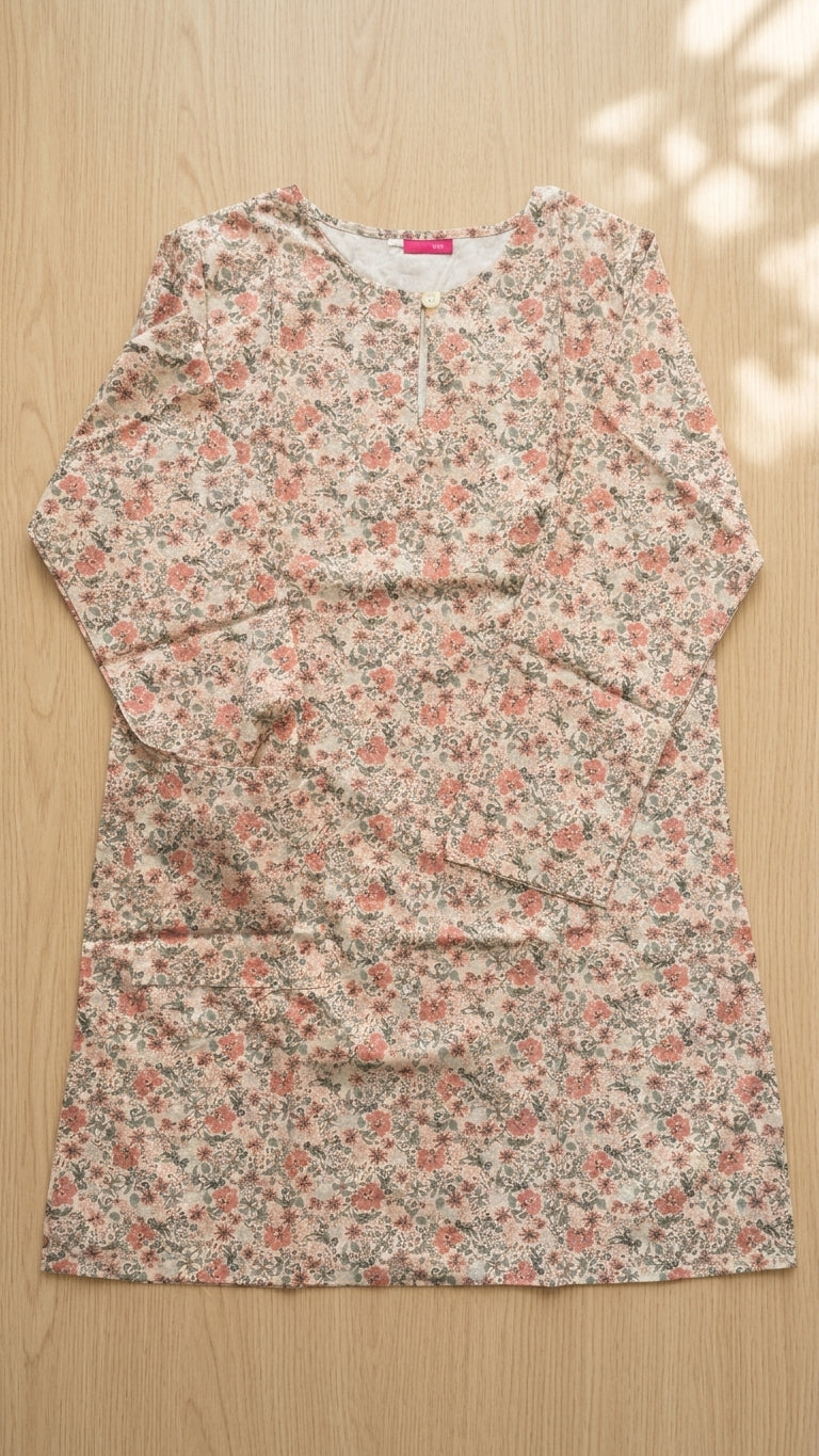 A long-sleeve tunic dress with a dense small floral print in pink, green, and beige, laid flat on a light wood background.