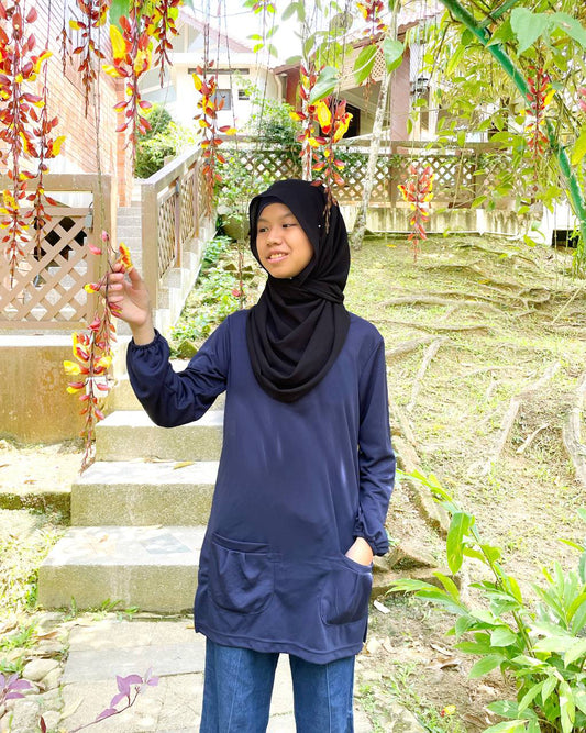 Person wearing a navy blue dry fit tee with a black hijab standing outdoors near steps and plants.