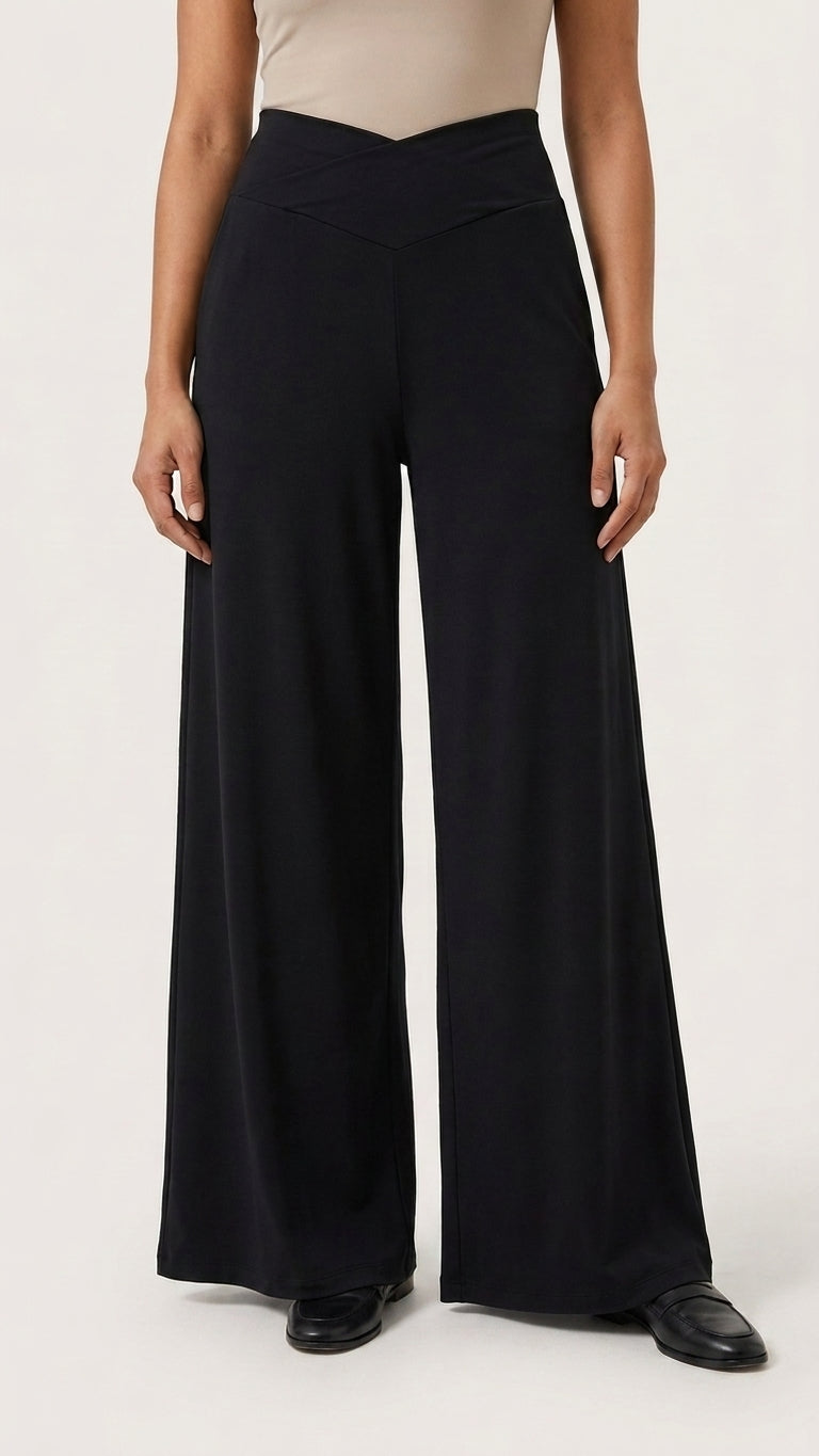 A model wearing black wide-leg cropped pants with a v-shape waistband, paired with a beige top and black loafers, shown against a plain light background.