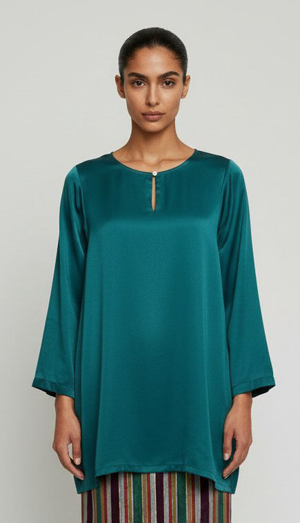 Woman wearing a teal long blouse with a plain background