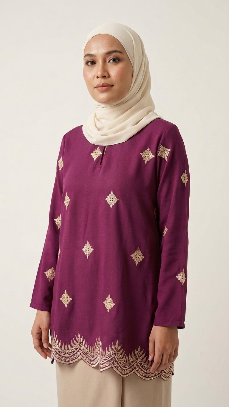 A woman wearing a long-sleeve purple tunic with gold geometric embroidery and a scalloped hem, paired with a cream hijab and light beige trousers, photographed against a plain light background.