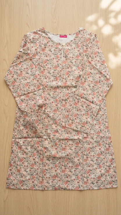 A long-sleeve tunic dress with a dense small floral print in pink, green, and beige, laid flat on a light wood background.