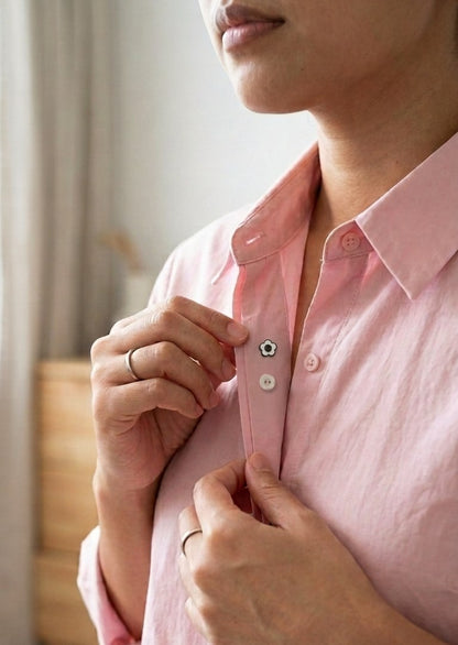 A close-up of a person wearing a light pink button-down shirt, adjusting the collar and front buttons with both hands.
