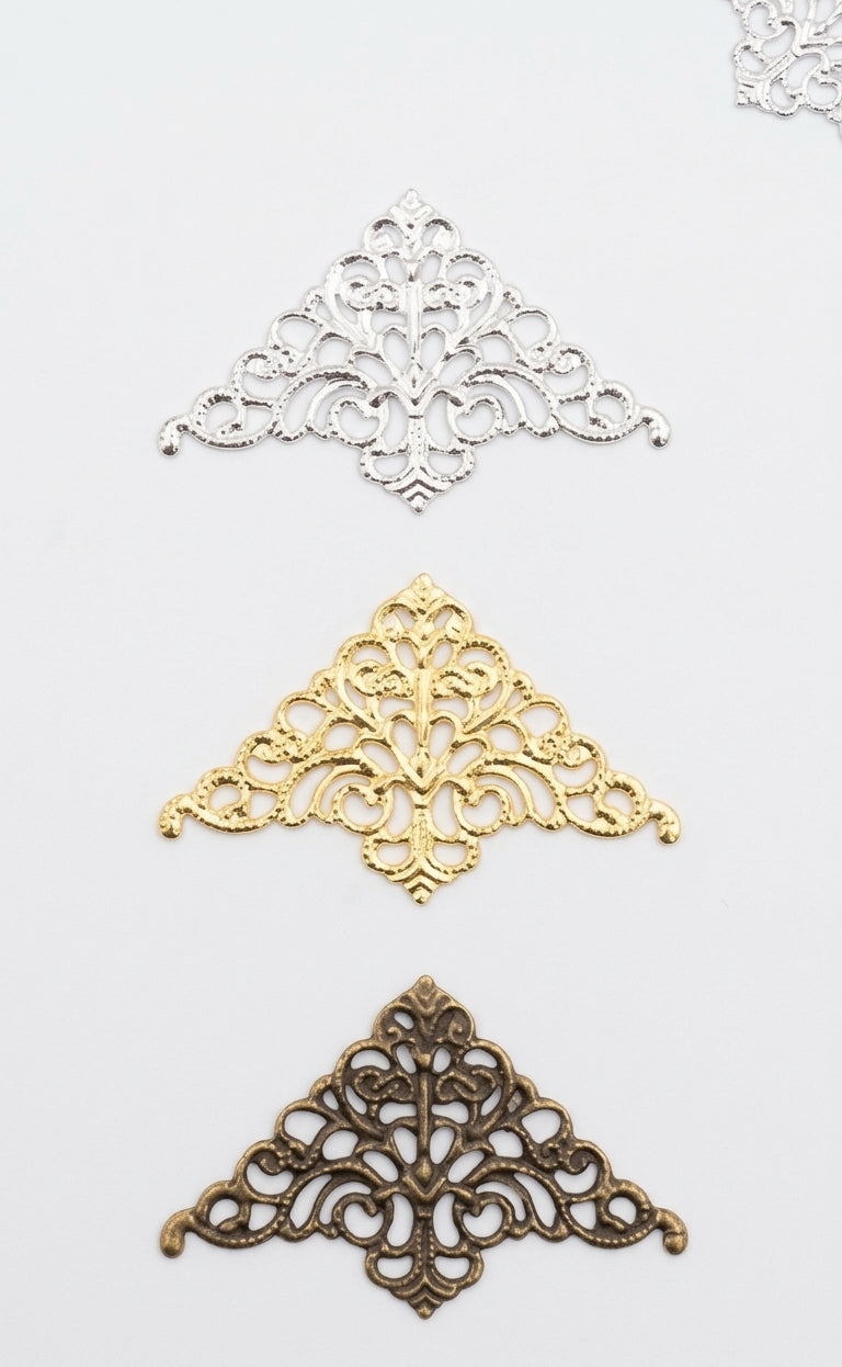 Three ornate filigree corner embellishments in silver, gold, and antique bronze finishes, arranged vertically on a plain white background.
