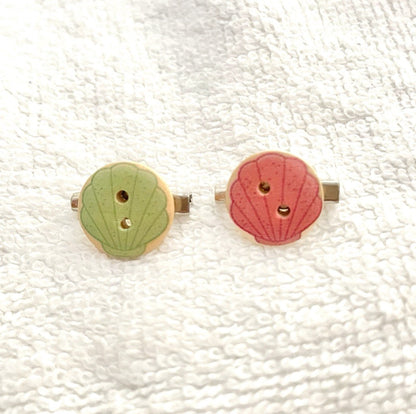 A pair of vintage-style wooden button earrings with scalloped edges, one in light green and one in dusty pink, both featuring gold-tone metal post backs, displayed on a textured white fabric background.