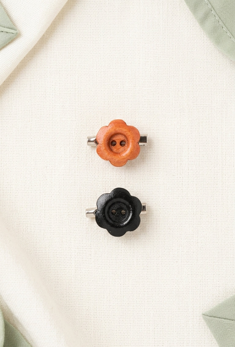 Two small flower-shaped metal buttons, one orange and one black, displayed on a textured cream fabric background.
