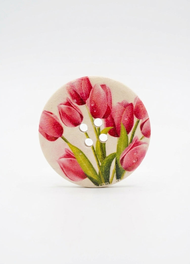 A round button featuring a printed design of pink tulips with green leaves on a light beige background, shown on a clean white studio background.