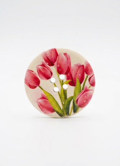 A round button featuring a printed design of pink tulips with green leaves on a light beige background, shown on a clean white studio background.