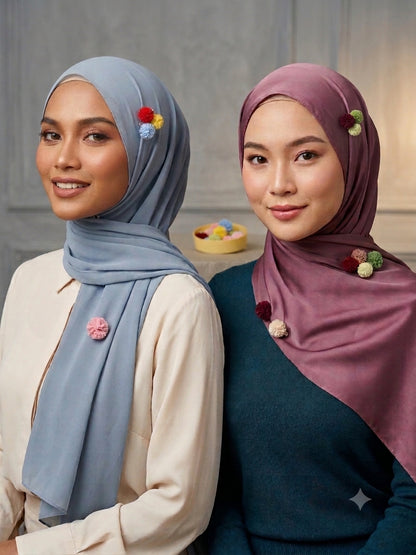 Two women wearing hijabs with decorative pins, one in gray and the other in purple, against a neutral background.