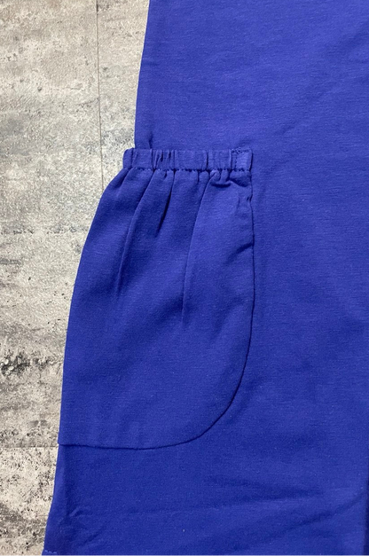 A close-up of a royal blue scrub top or dress with an elasticized pocket opening, laid flat on a textured gray concrete surface.