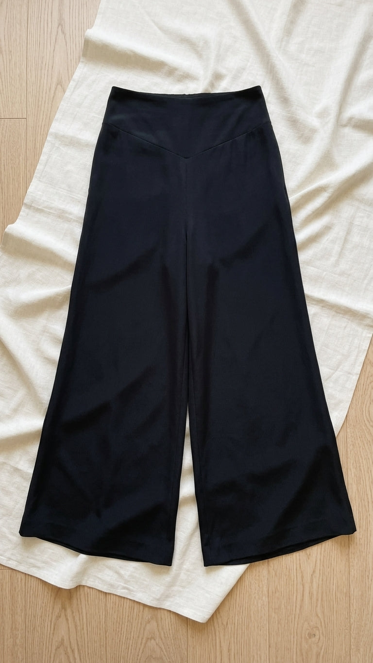 Black wide-leg cropped pants laid flat on a cream-colored fabric sheet over a light wood floor.