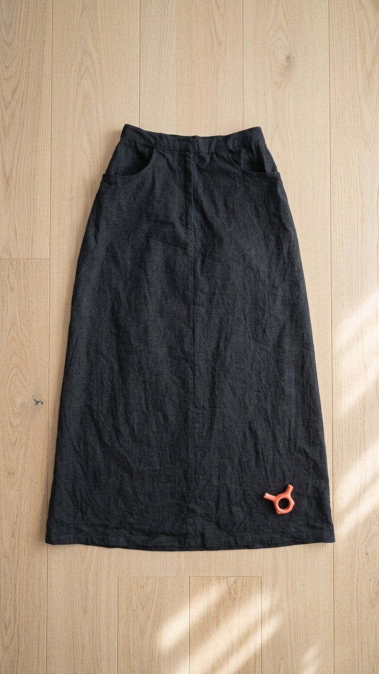 A black denim long skirt laid flat on a light wood floor with soft window shadows.