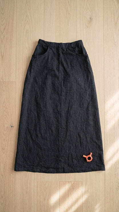 A black denim long skirt laid flat on a light wood floor with soft window shadows.