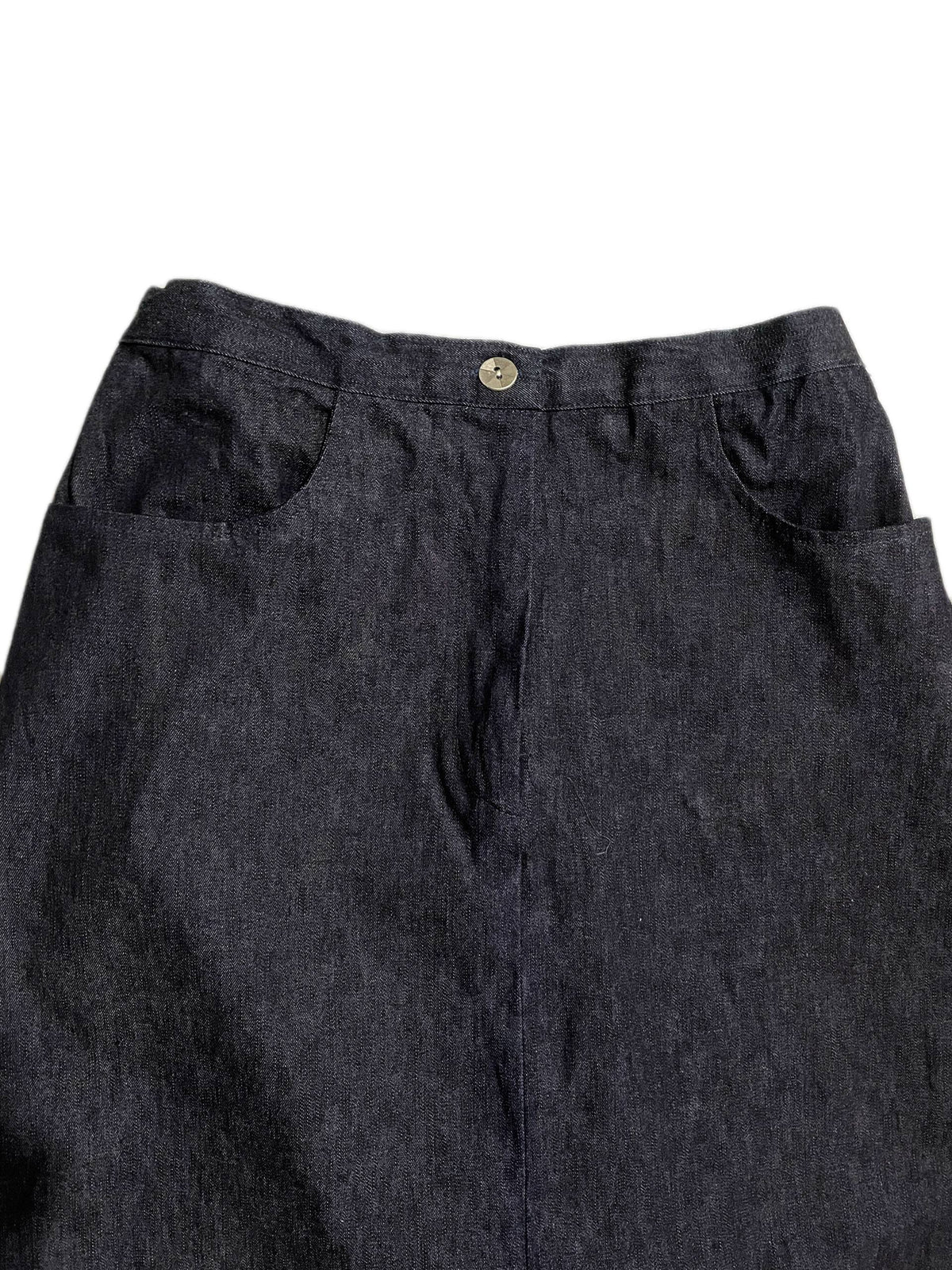 Close-up of the waistband and upper front of dark indigo blue denim skirt, showing a single metal button and side pocket seams against a plain white background.