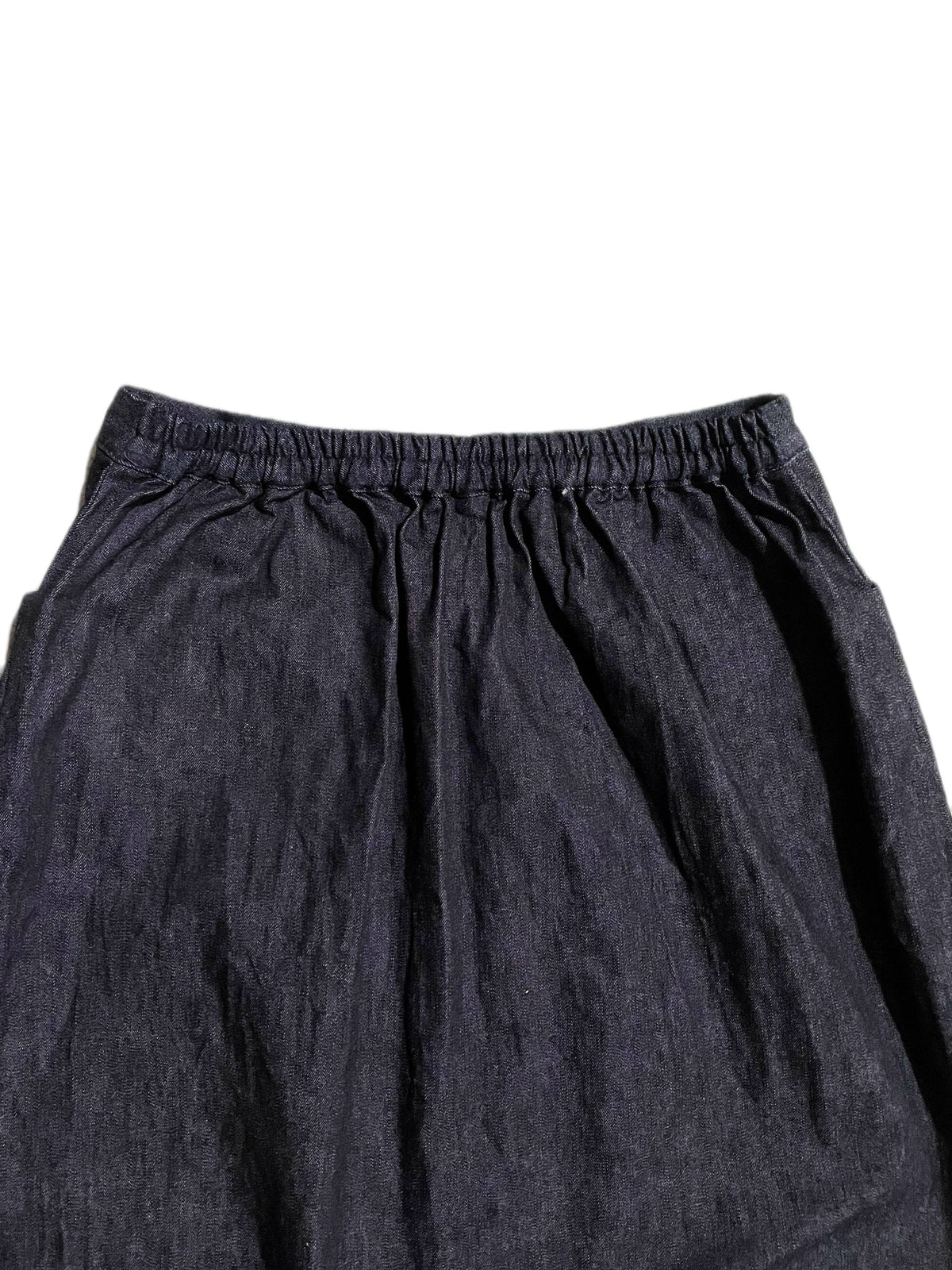 Close-up of a dark indigo blue denim skirt, showing an elastic waistband and gathered folds against a plain white background.