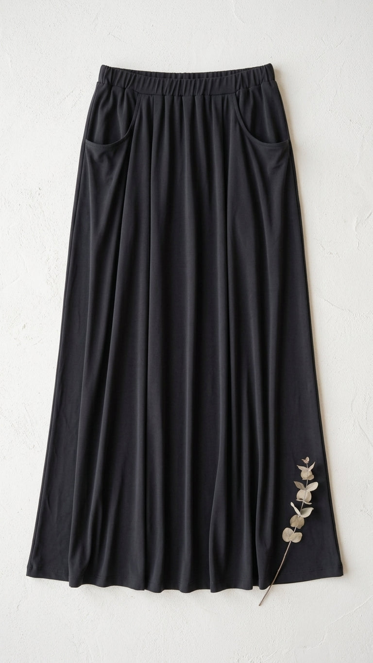 A black midi skirt with an elastic waistband, front pockets displayed flat against a textured off-white background.