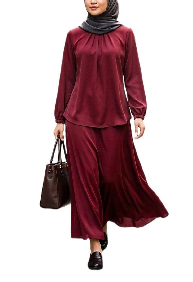 A woman modeling a two-piece maroon long-sleeve top and matching max skirt set, paired with a dark gray hijab, black loafers, and carrying a dark brown tote bag against a plain white background.