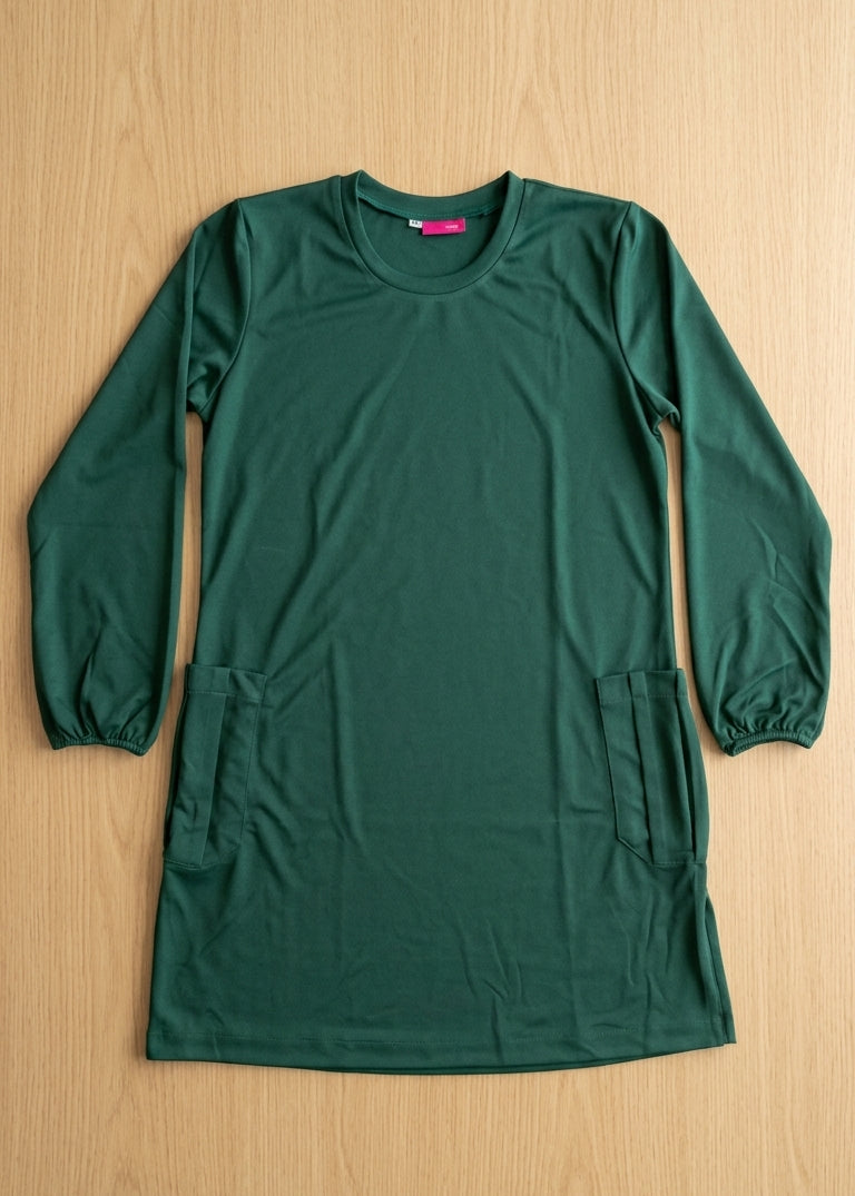 A dark green long-sleeve tunic dress with elastic cuffs and two front patch pockets, laid flat on a light wood background.