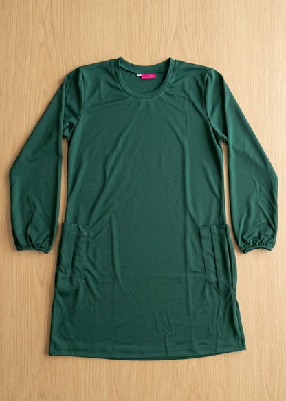 A dark green long-sleeve tunic dress with elastic cuffs and two front patch pockets, laid flat on a light wood background.